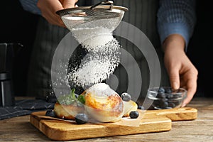 Woman sieving sugar powder on cottage cheese pancakes at wooden table