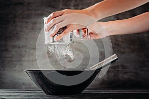 Woman sifting flour with sieve in black bowl