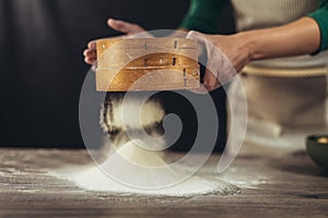 Woman sifting flour through a sieve on the wooden table