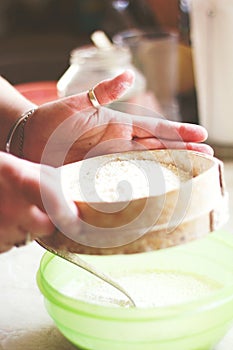 Woman sifting flour for yeast dough in kitchen