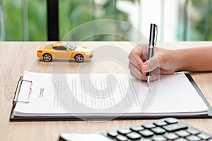 Woman signing car loan agreement contract with car toy and calculator on wooden desk.