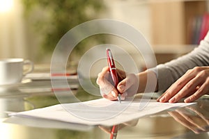 Woman signing document with pen on a desk at home