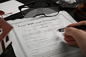 Woman signing last will and testament at black table, closeup