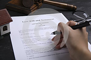 Woman signing last will and testament at black table, closeup