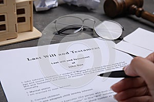 Woman signing last will and testament at grey table, closeup