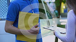 Woman signing proof delivery form and receiving yellow package from courier