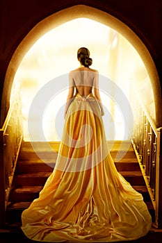 Woman Silhouette in Golden Luxury Gown. Elegant Lady in Yellow Long Silk Dress with naked Back Rear Side View looking at Light