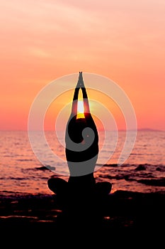 Woman silhouette sitting in yoga pose on sea background back lit