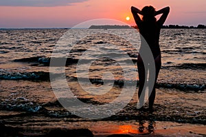 Woman silhouette in swimsuit with raised arms looking at amazing sunrise near sea