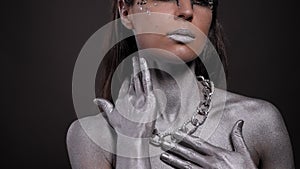 Woman with silver paint on her skin, face and hair poses in a studio with chain.