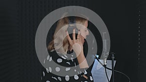 Woman singer in headphones singing in microphone recording song in sound studio.