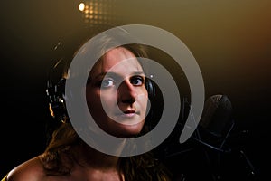 Woman singer looking at the camera at the recording Studio, black background. Portrait of a girl in large headphones with a