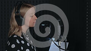 Woman singer puts off headphones ending singing in microphone recording song.