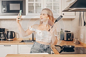 Woman singing and dancing in the kitchen with a smartphone, music.A girl in headphones with a phone stands in the kitchen and