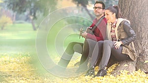 Woman singing and man playing guitar while sitting on a tree in park