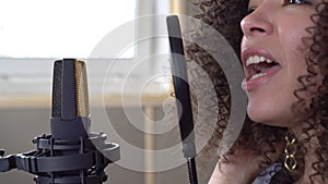 Woman singing into a microphone in a recording studio, face close-up