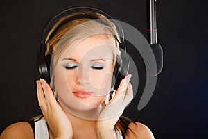Woman singing to microphone wearing headphones in studio