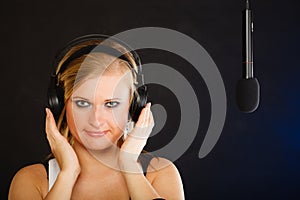 Woman singing to microphone wearing headphones in studio