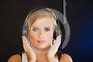 Woman singing to microphone wearing headphones in studio