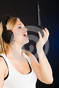 Woman singing to microphone wearing headphones in studio