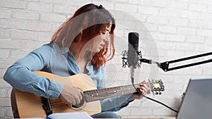 A woman sings into a microphone and plays the guitar live on a laptop. Girl musician recording a video blog