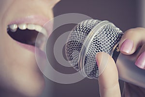 A woman sings into a microphone at a recording studio, her mouth close up.