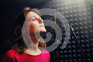Woman sings into a recording studio on black background. Professional female vocalists in red clothes. Recording singer at a