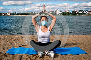 Woman in singular mask do yoga on the beach