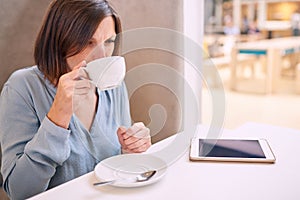 Woman sipping cappaccino in a bright cafe with tablet photo