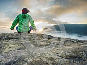 Woman sit on cliff edge and looking to rising sun above mist