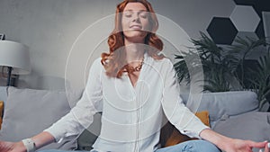 Woman sit cross legged on sofa in living room closed eyes do meditation practice