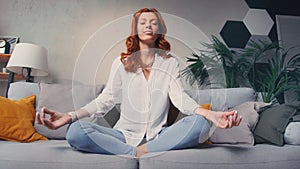 Woman sit cross legged on sofa in living room closed eyes do meditation practice