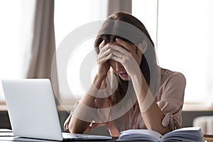 Woman sit at desk holding head with hands feels stressed