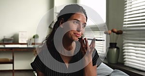 Woman sit indoors chatting with friend by smartphone using speakerphone