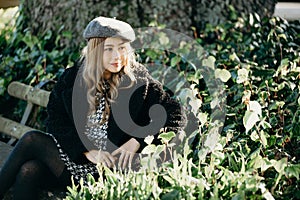 Woman sit on a park bench, leisure time in autumn park. fashion woman in black coat sitting on a bench