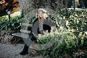 Woman sit on a park bench, leisure time in autumn park. fashion woman in black coat sitting on a bench