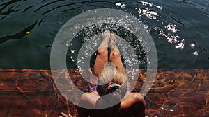 Woman sit on a pier in sunglasses and swimming suit. Girl rest on a flood wood underwater pier. Lady in the water and