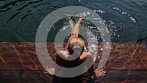 Woman sit on a pier in sunglasses and swimming suit. Girl rest on a flood wood underwater pier. Lady in the water and