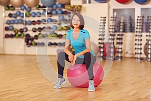 Woman sit on a pink Pilates ball indoors gym background.