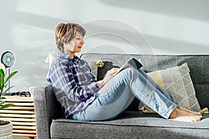 Woman sit on the sofa couch and relax while reading a book at home in cozy modern interior living room with green plants