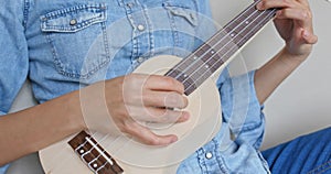 Woman sit on sofa and play with ukulele