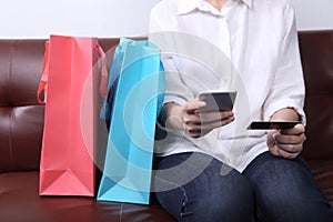 Woman sit on sofa with shopping bag use smarth phone with paying
