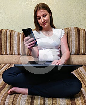 Woman sit on sofa, use laptop and smartphone