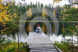 Young woman sit on dock enjoying landscape of autumn forest, lake with colored yellow golden trees