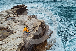 woman siting on the edge of the cliff looking on big waves