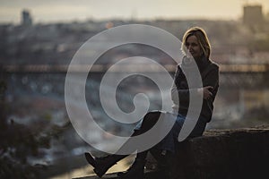 A woman sits an ancient stone wall at dusk in Porto, Portugal.