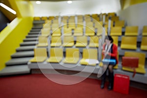 Woman sits in auditorium with yellow chairs, image photo
