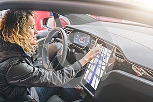 Woman sits behind wheel in car and uses electronic dashboard. Girl traveler looking for way through navigation system.