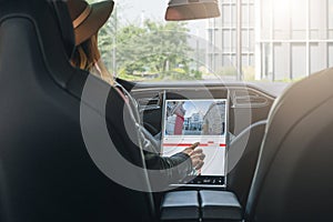 Woman sits behind wheel in car and uses electronic dashboard. Girl traveler looking for way through navigation system.