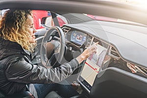 Woman sits behind wheel in car and uses electronic dashboard. Girl traveler looking for way through navigation system.